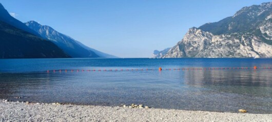 il lago di garda al mattino con un cielo terso e l'acqua calmissima e di un bellissimo colore azzurro, spiaggia di sassi bianchi